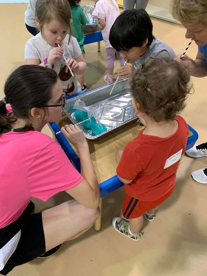Adults and children blowing through straws into a foil pan