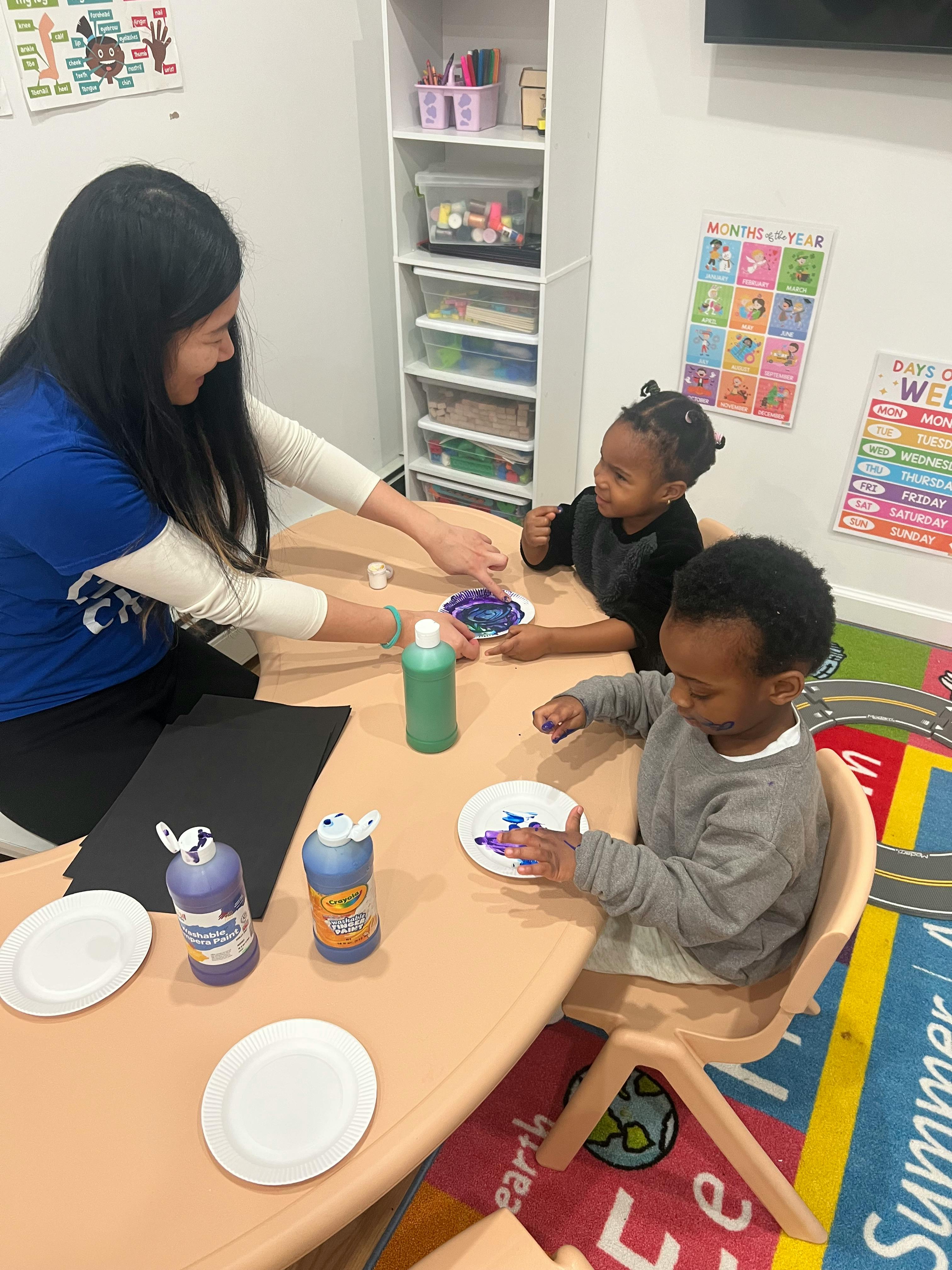Person and two children finger painting at a table