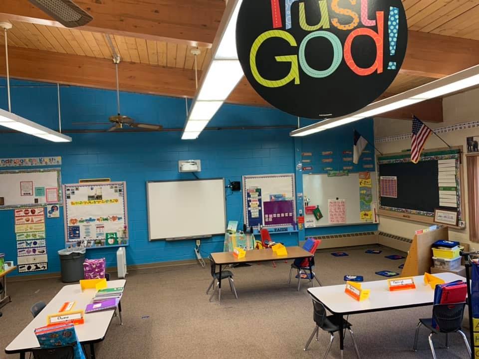 Classroom with tables, chairs, whiteboards, and a sign that reads "Trust God!"