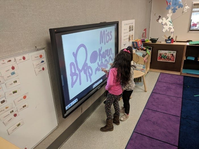 Two children drawing on an interactive whiteboard in a classroom