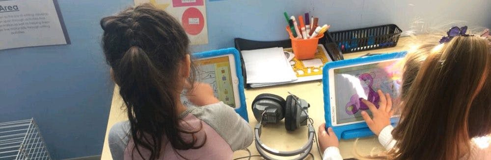 Two children using tablets at a desk