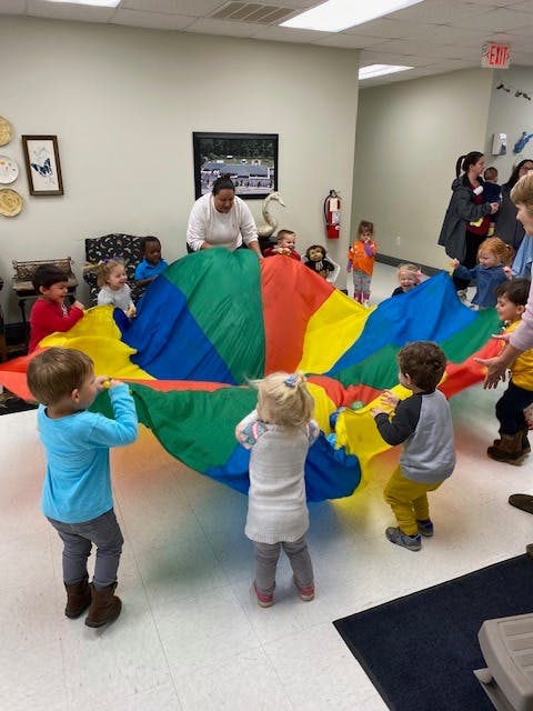 Adult and children playing with a colorful parachute indoors