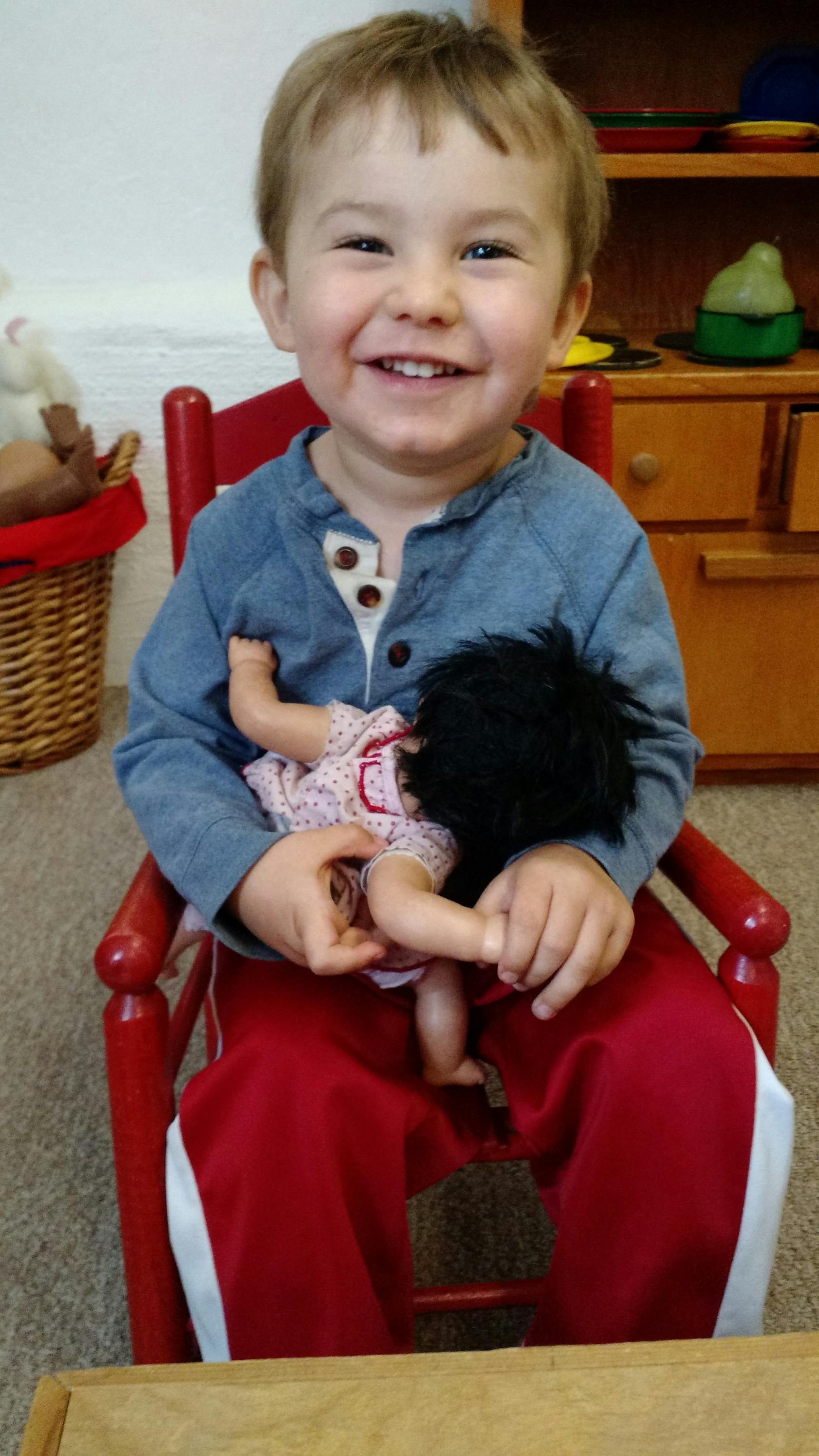Child sitting in a red chair holding a doll