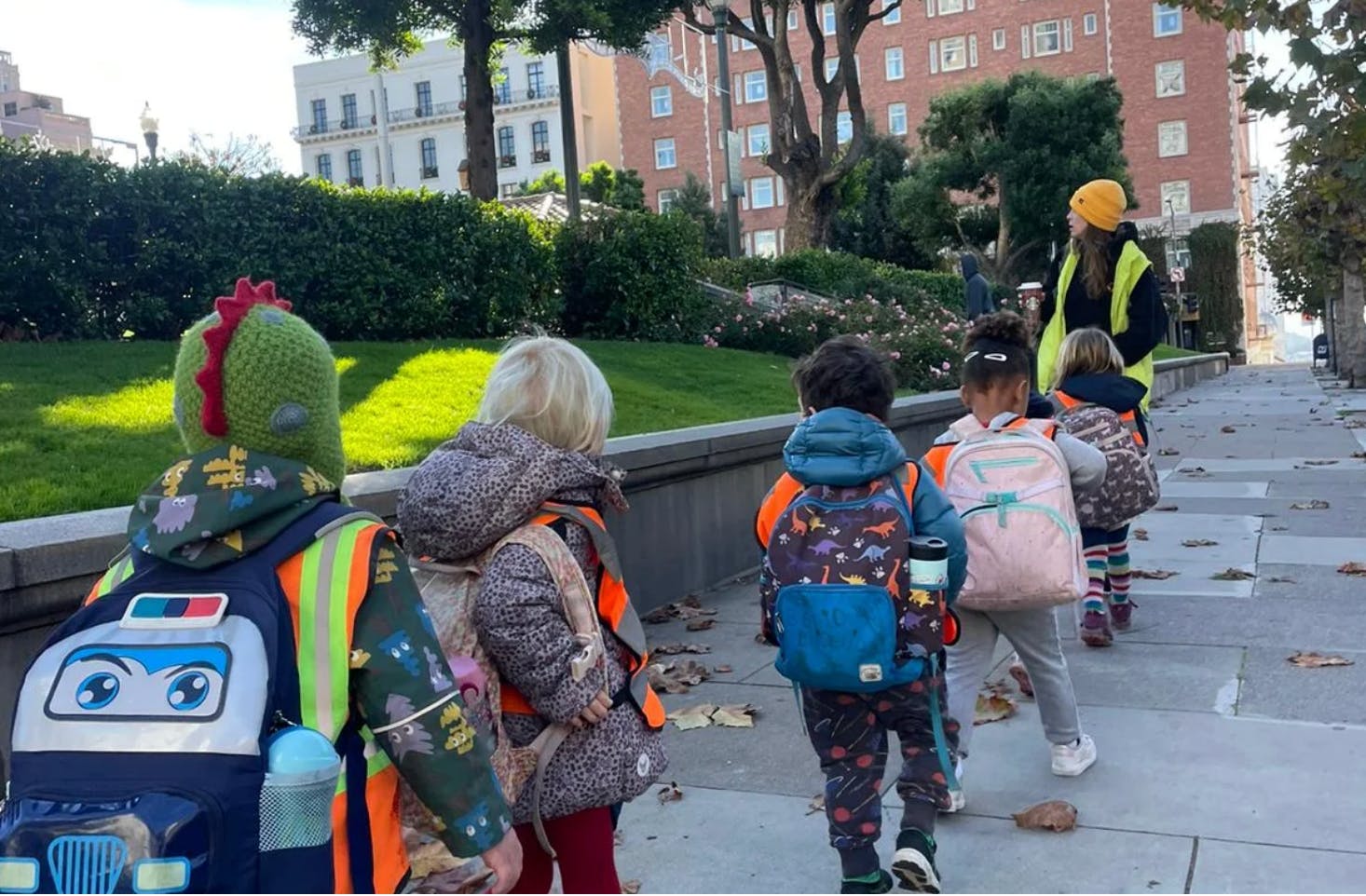 Children with backpacks walking on a sidewalk with an adult