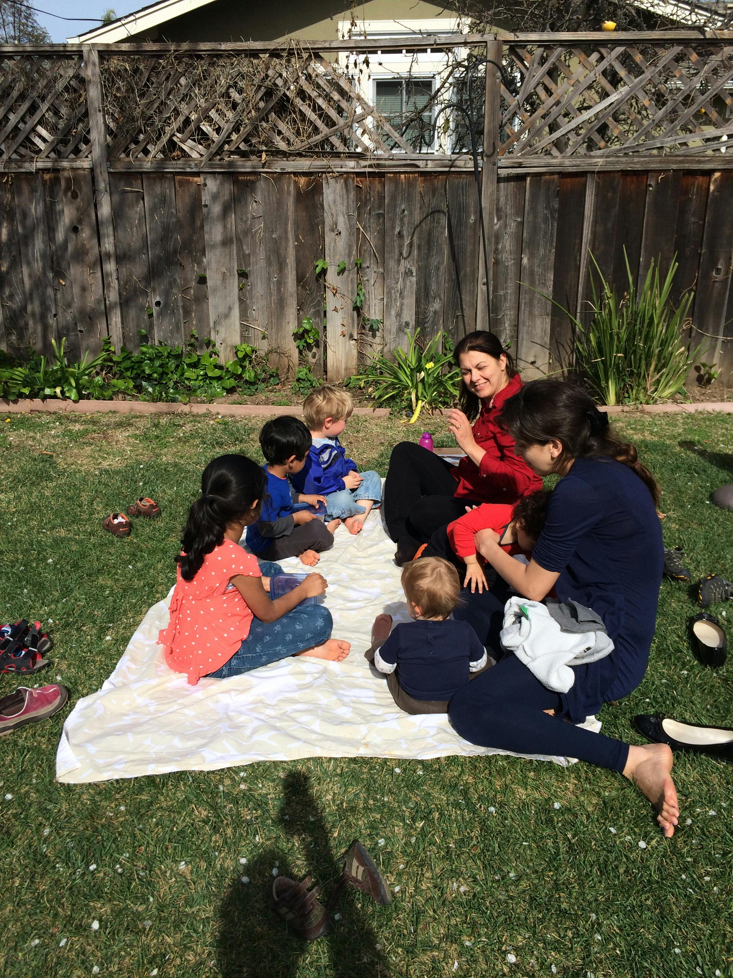 Two people and four children sitting on a blanket on grass