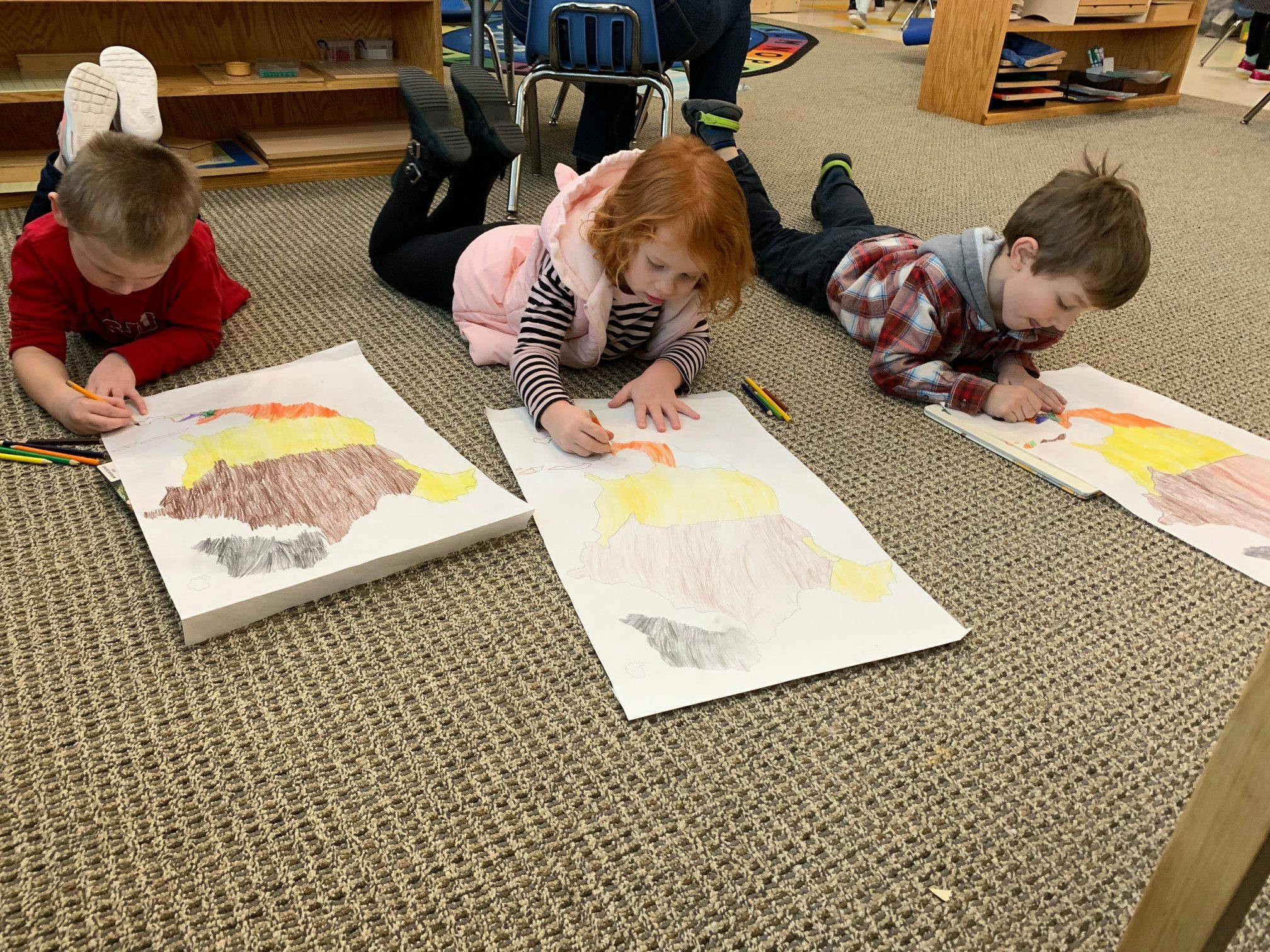 Three children lying on the floor drawing on paper