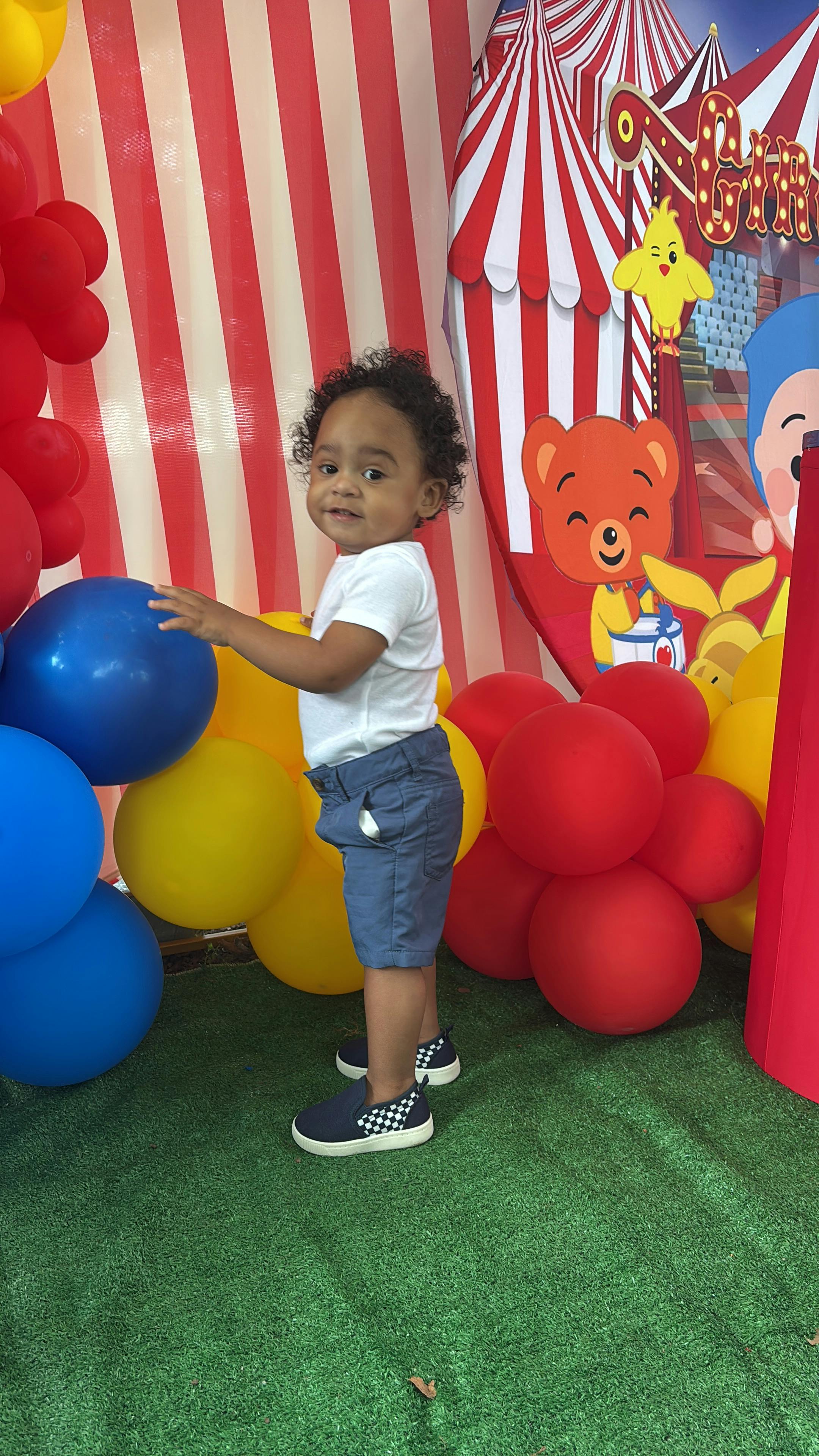 A young child standing next to colorful balloons with carnival themed decor