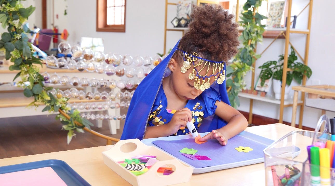 Child in blue outfit gluing shapes onto paper