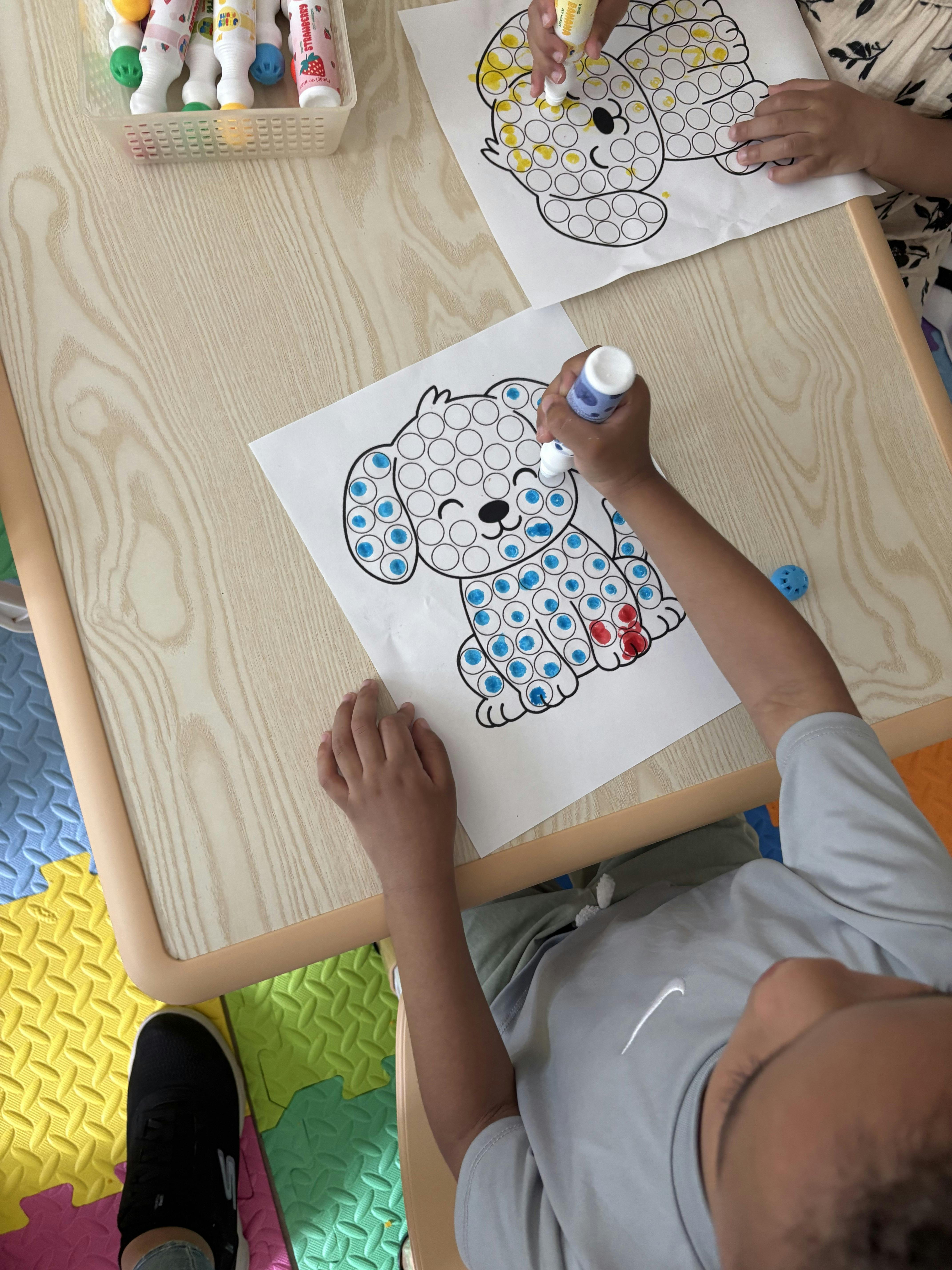 People using dot markers on dog coloring pages at a table