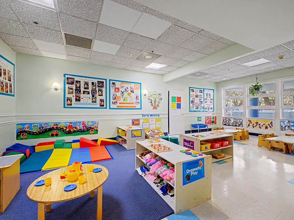 Classroom with playmats, small tables and chairs, and toy shelves