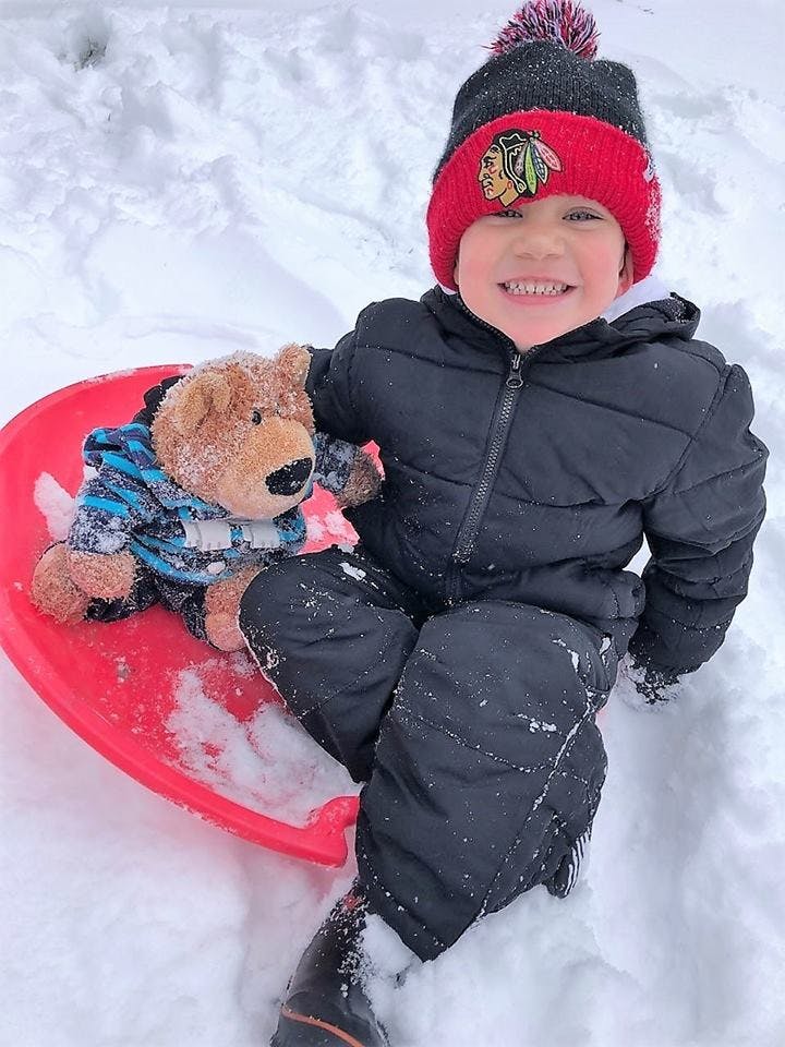 Child and teddy bear on a red sled in the snow