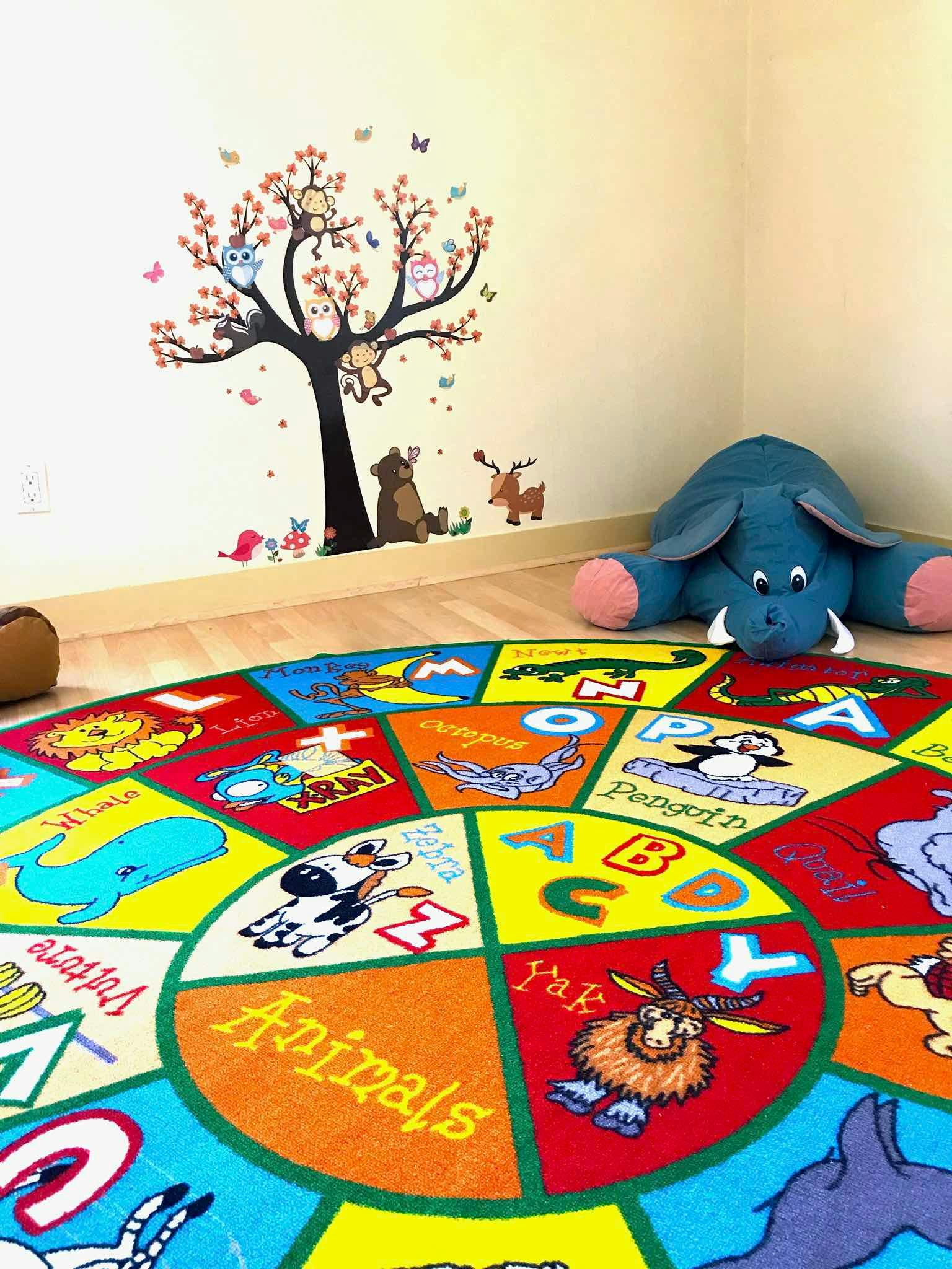 Colorful alphabet rug with animal illustrations in a room with a wall decal