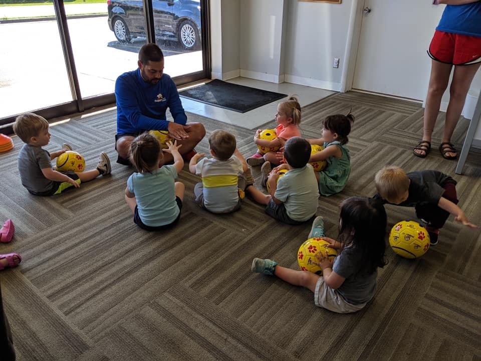 Person sitting on floor with children around ten children sitting around them