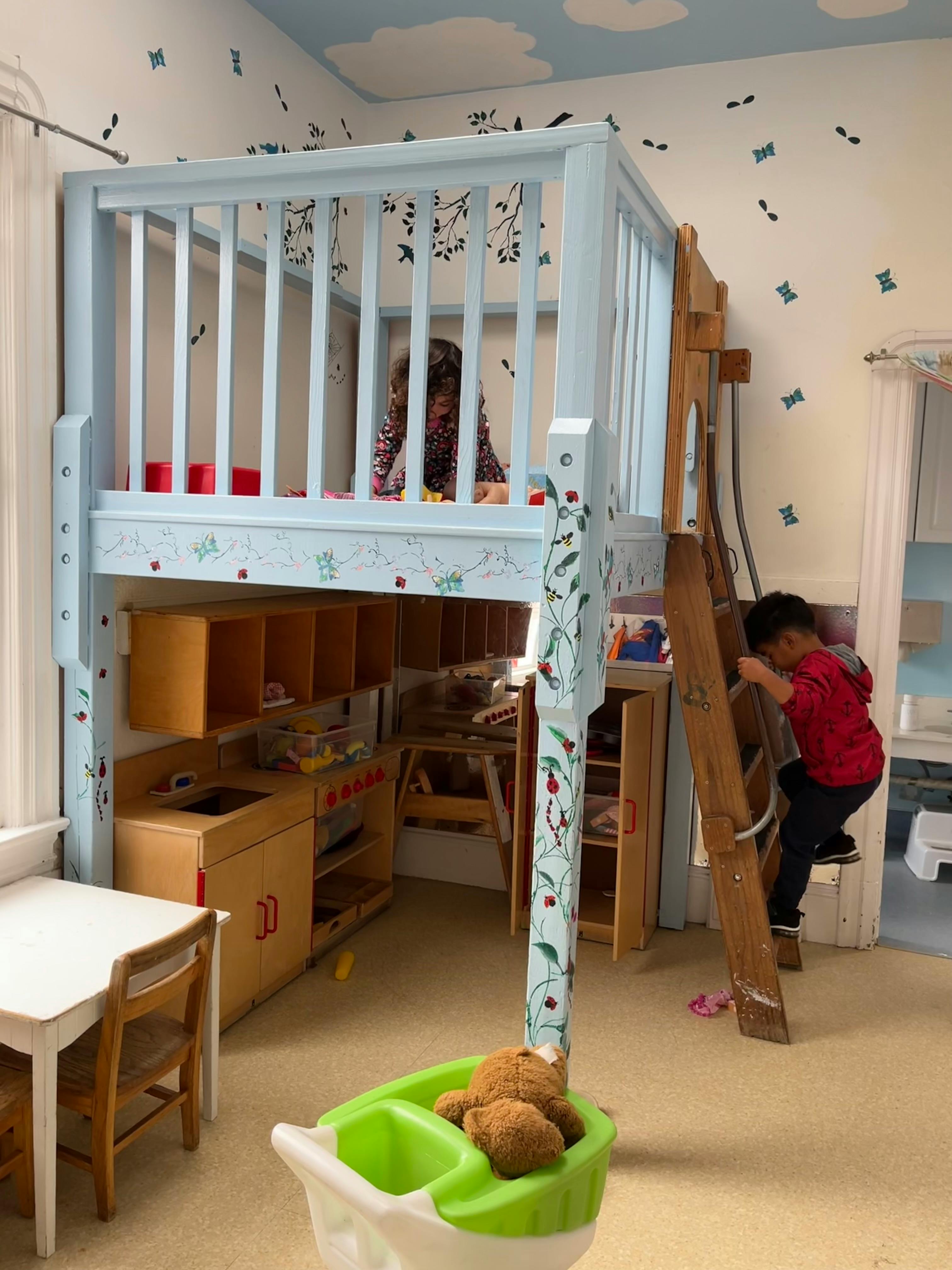 Child climbing a ladder to a play loft, another child in the loft
