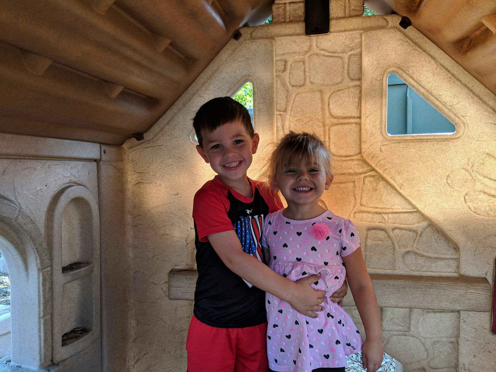 Two children smiling and embracing in a playhouse