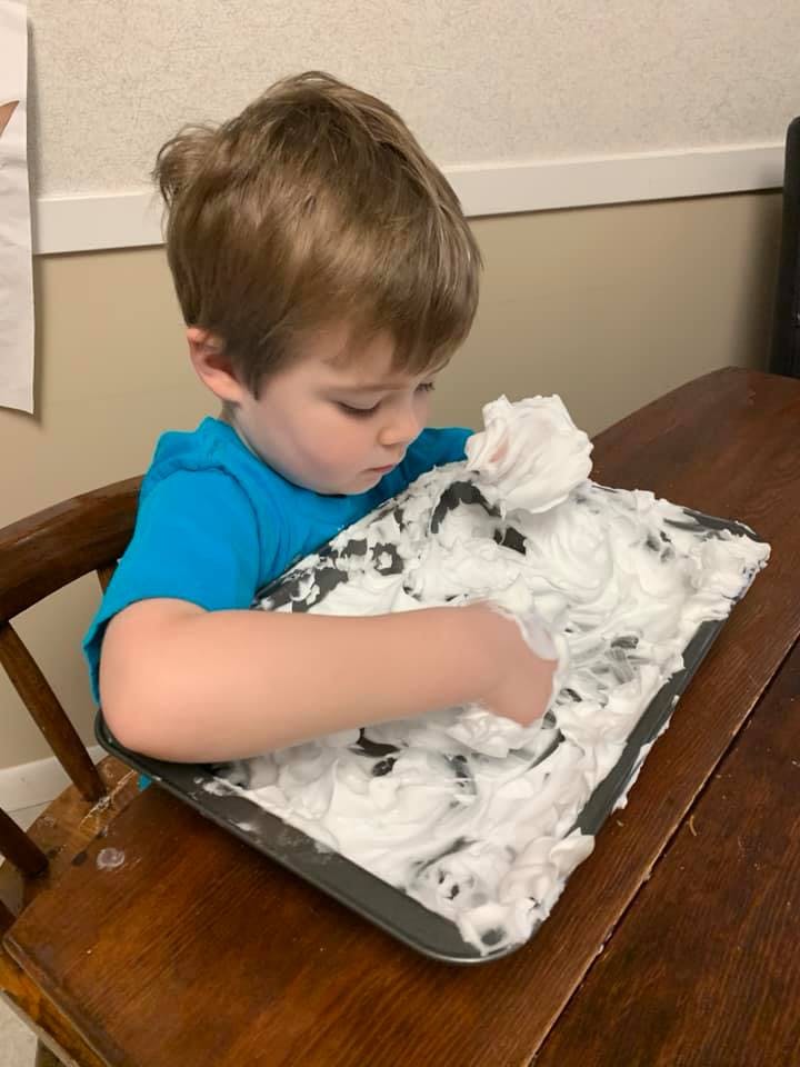 Child playing with shaving cream on a tray