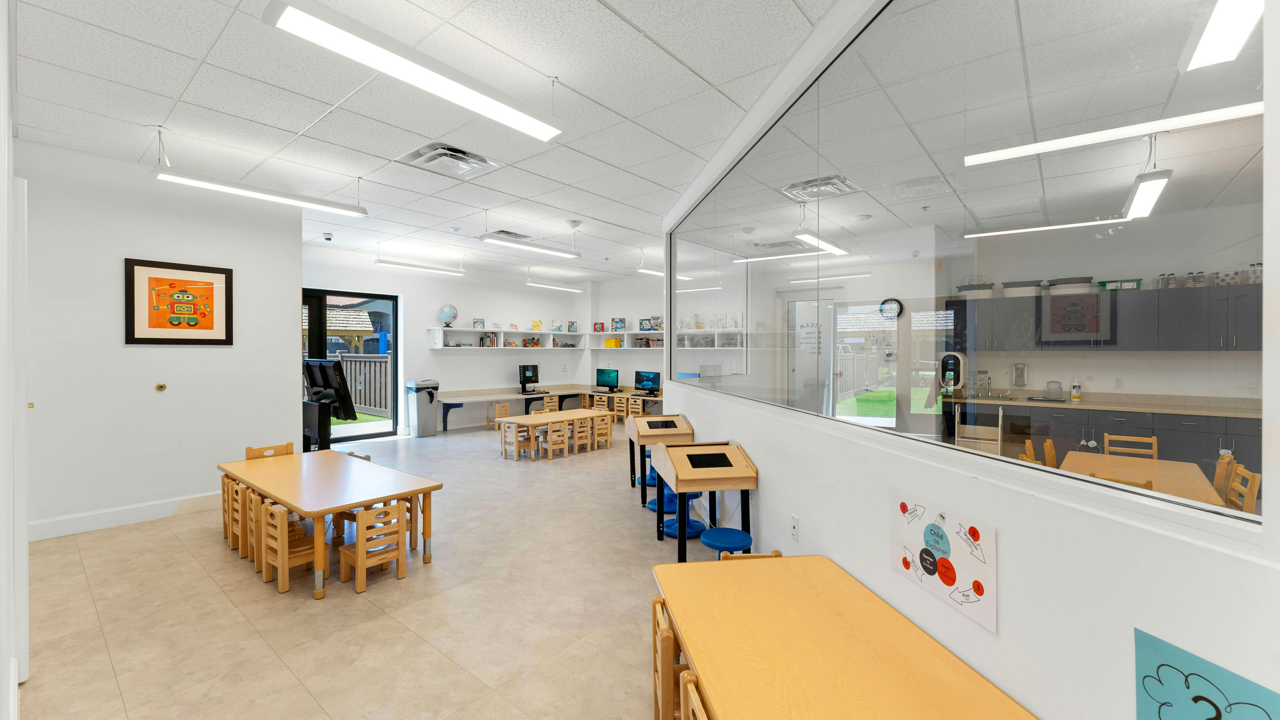 Classroom with tables, chairs, computer stations, and a separate kitchen area