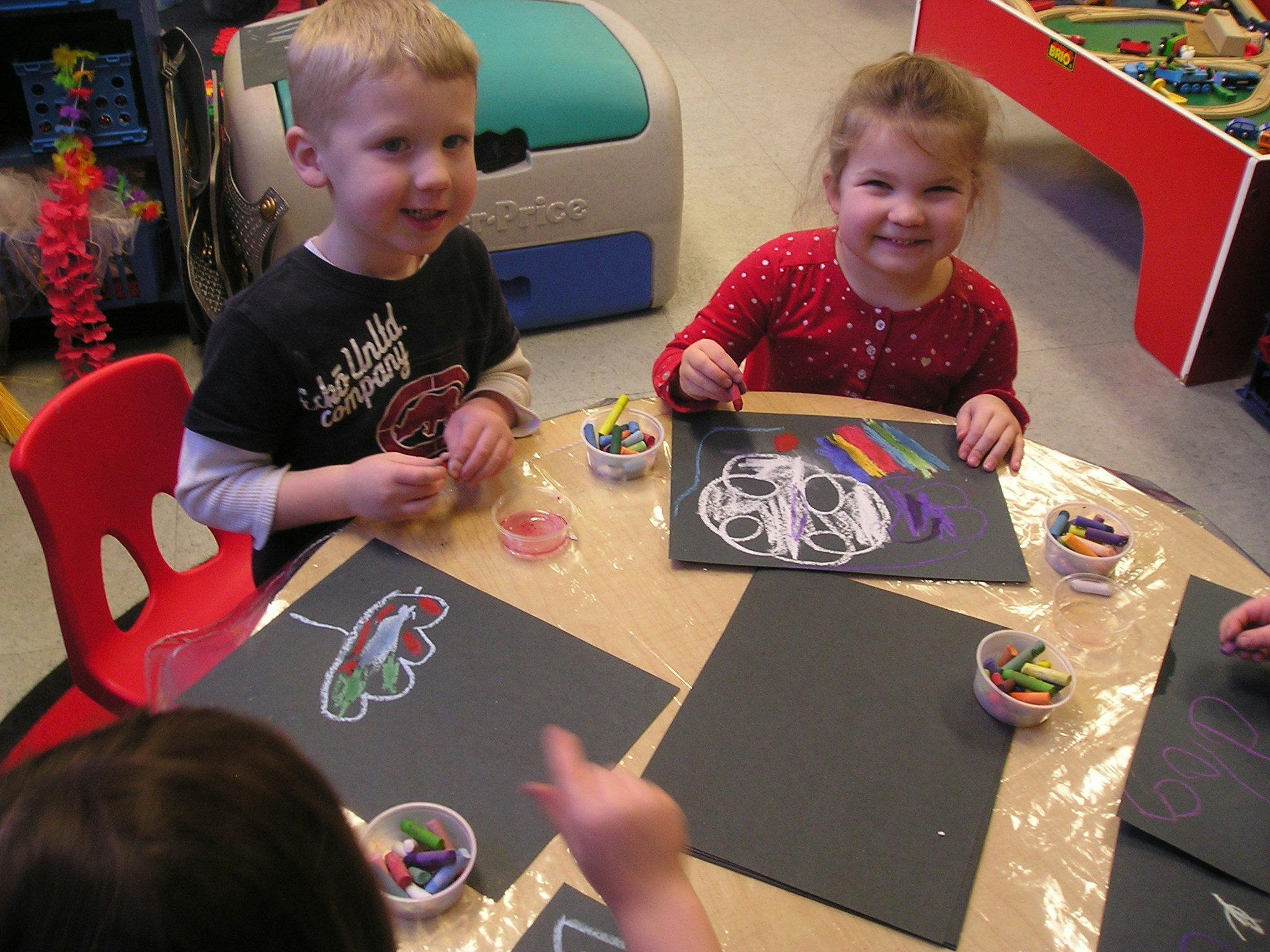 Two children drawing at a table with crayons
