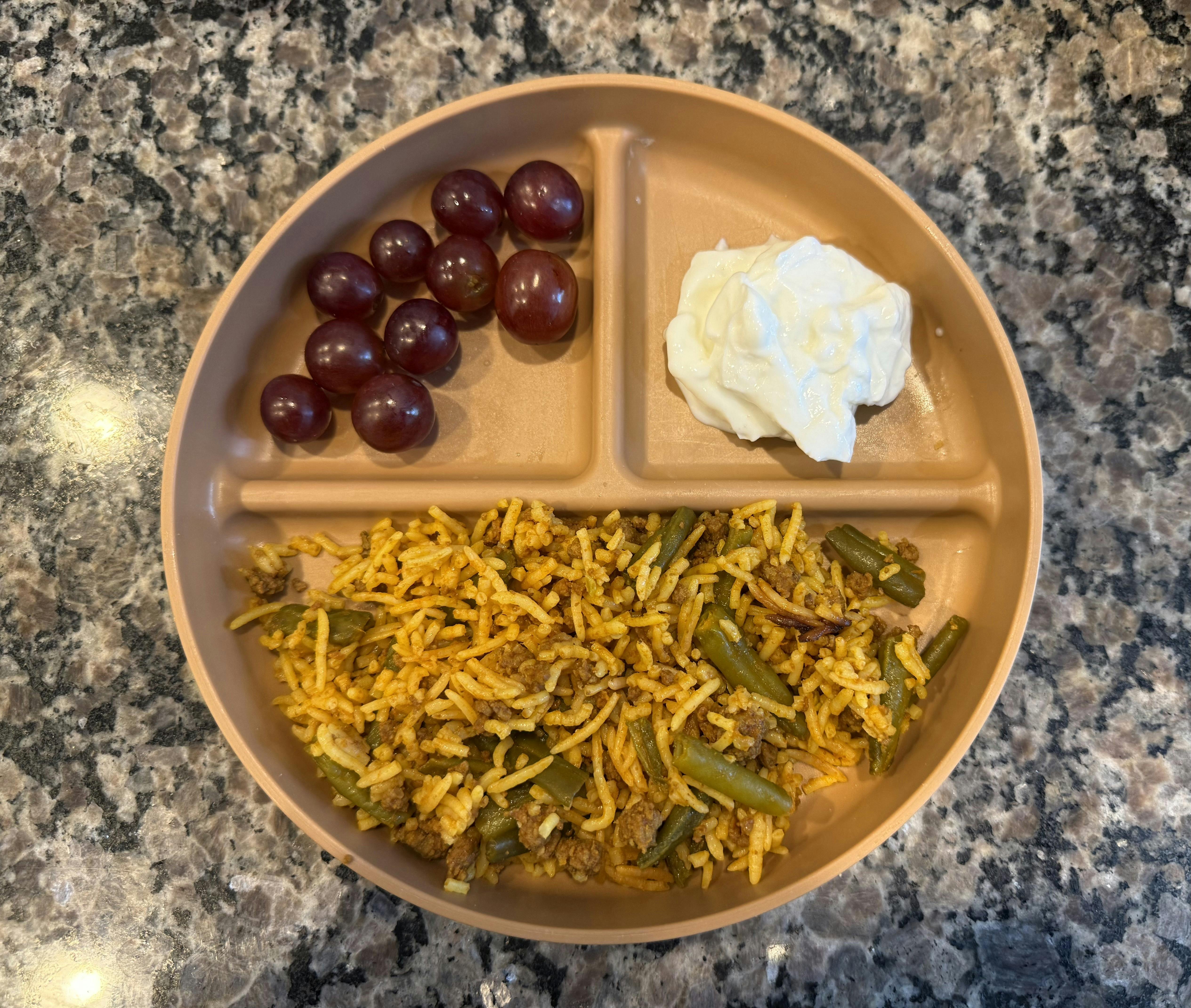 A divided plate with rice and green beans, red grapes, and yogurt
