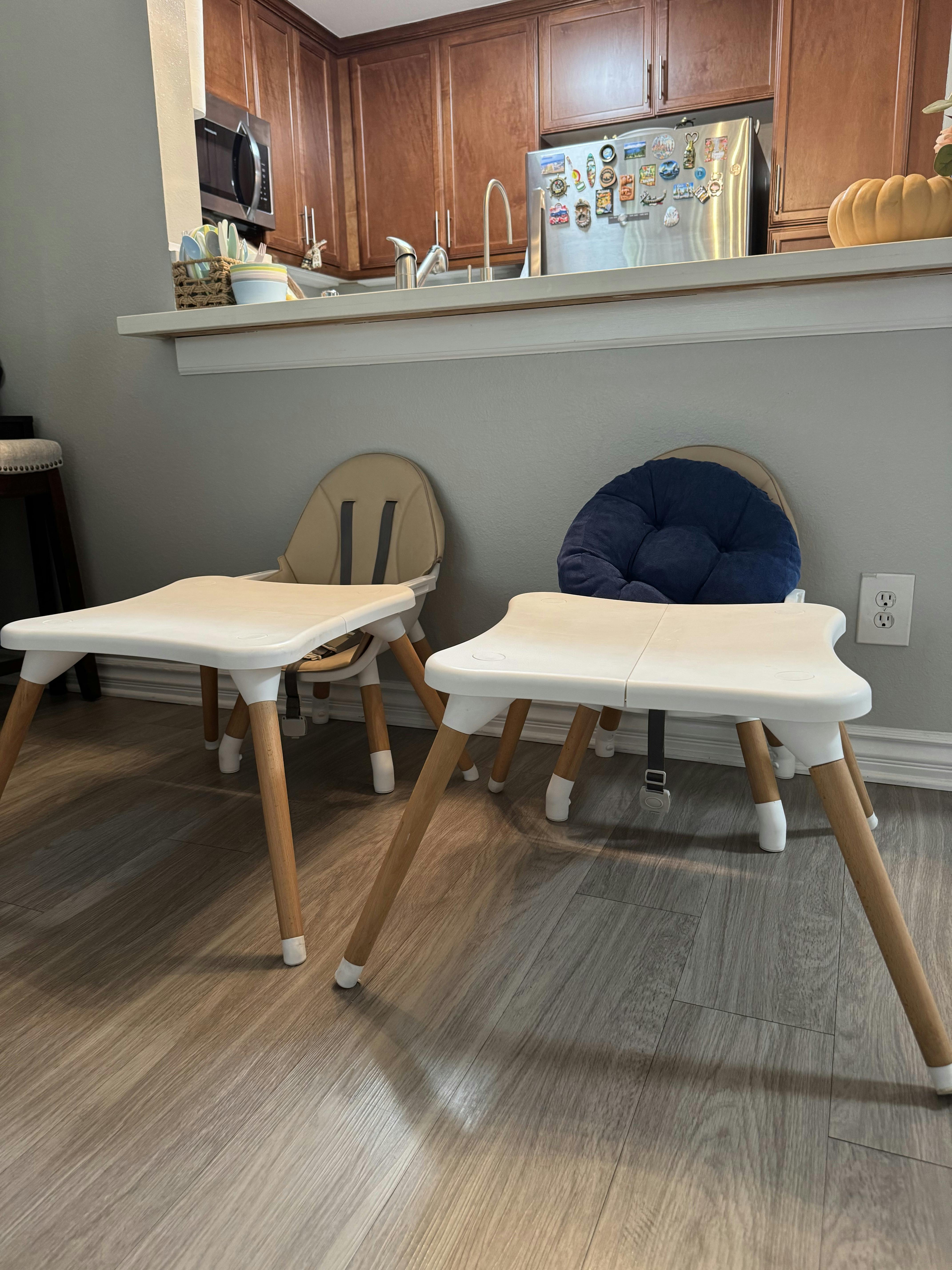 Two child high chairs with trays placed on a wood floor in a kitchen