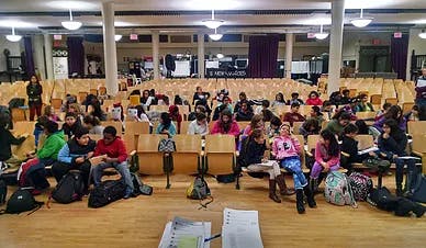 Many children and teens sitting in rows of chairs in a large room