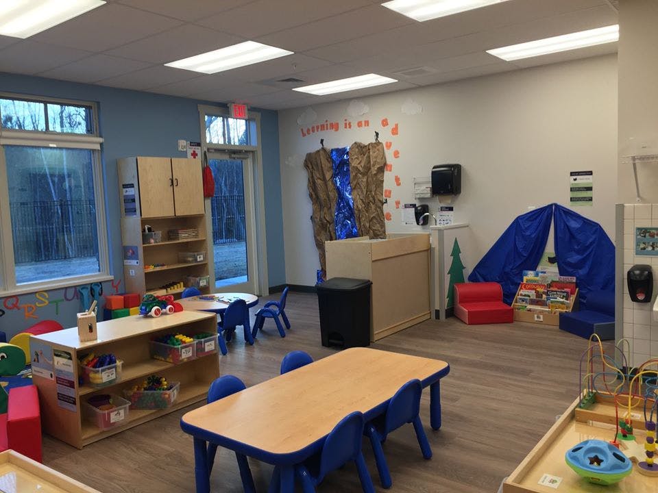Classroom with small tables and chairs, shelves with toys, and a blue tent
