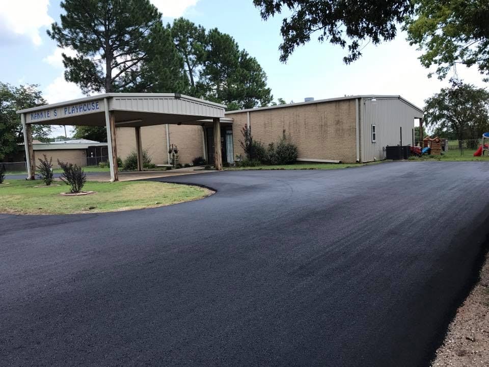 Freshly paved asphalt driveway leading to a building with a covered entrance