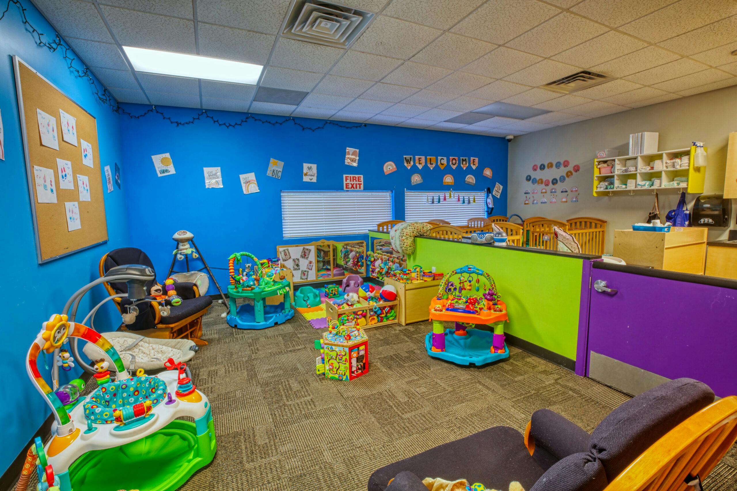 Colorful playroom with cribs, various children's toys, and infant seats