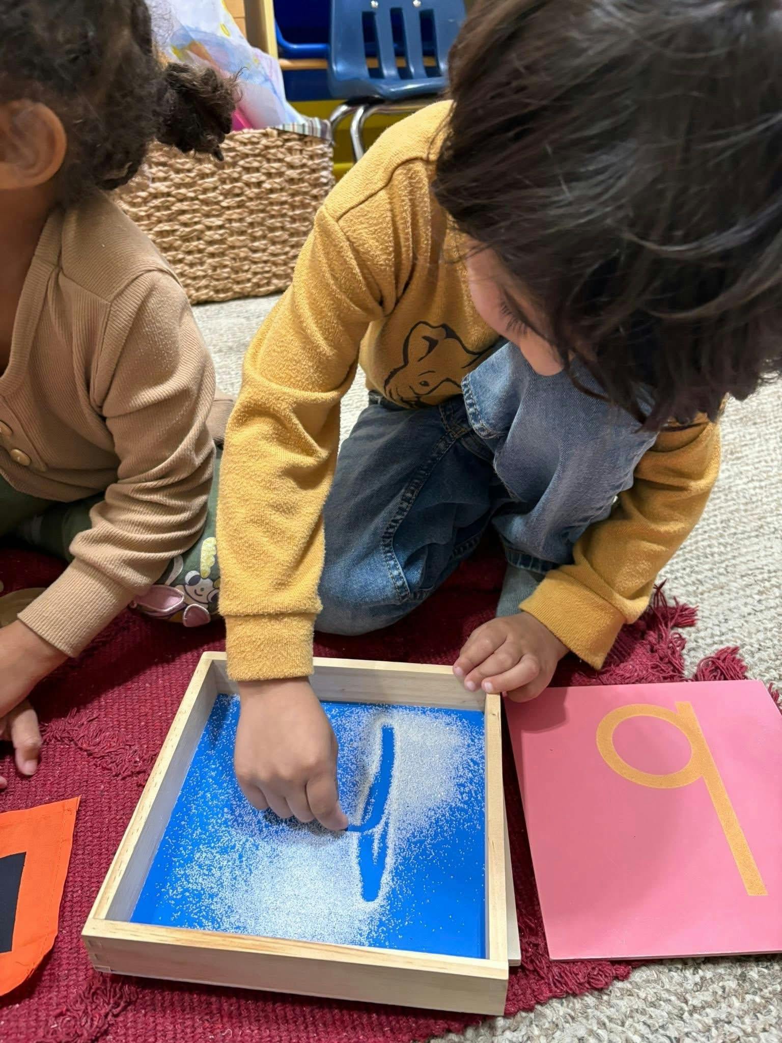 Child tracing a letter in a sand tray in a classroom