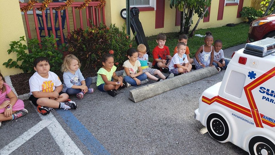 Children sitting on pavement looking at a toy ambulance