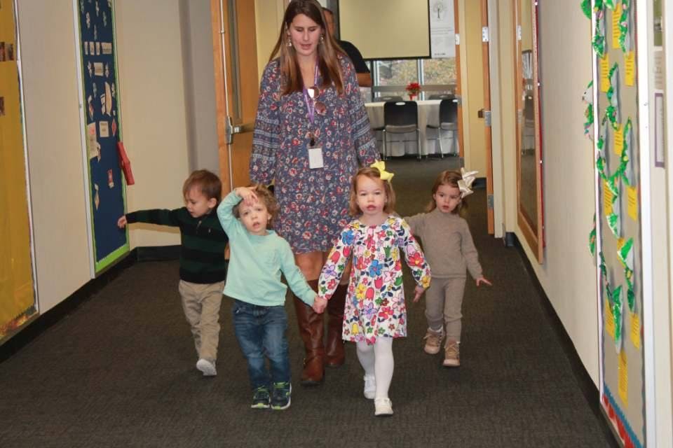 Adult person walking with three children in a hallway