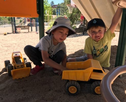 Two children playing with toy trucks in a sandbox
