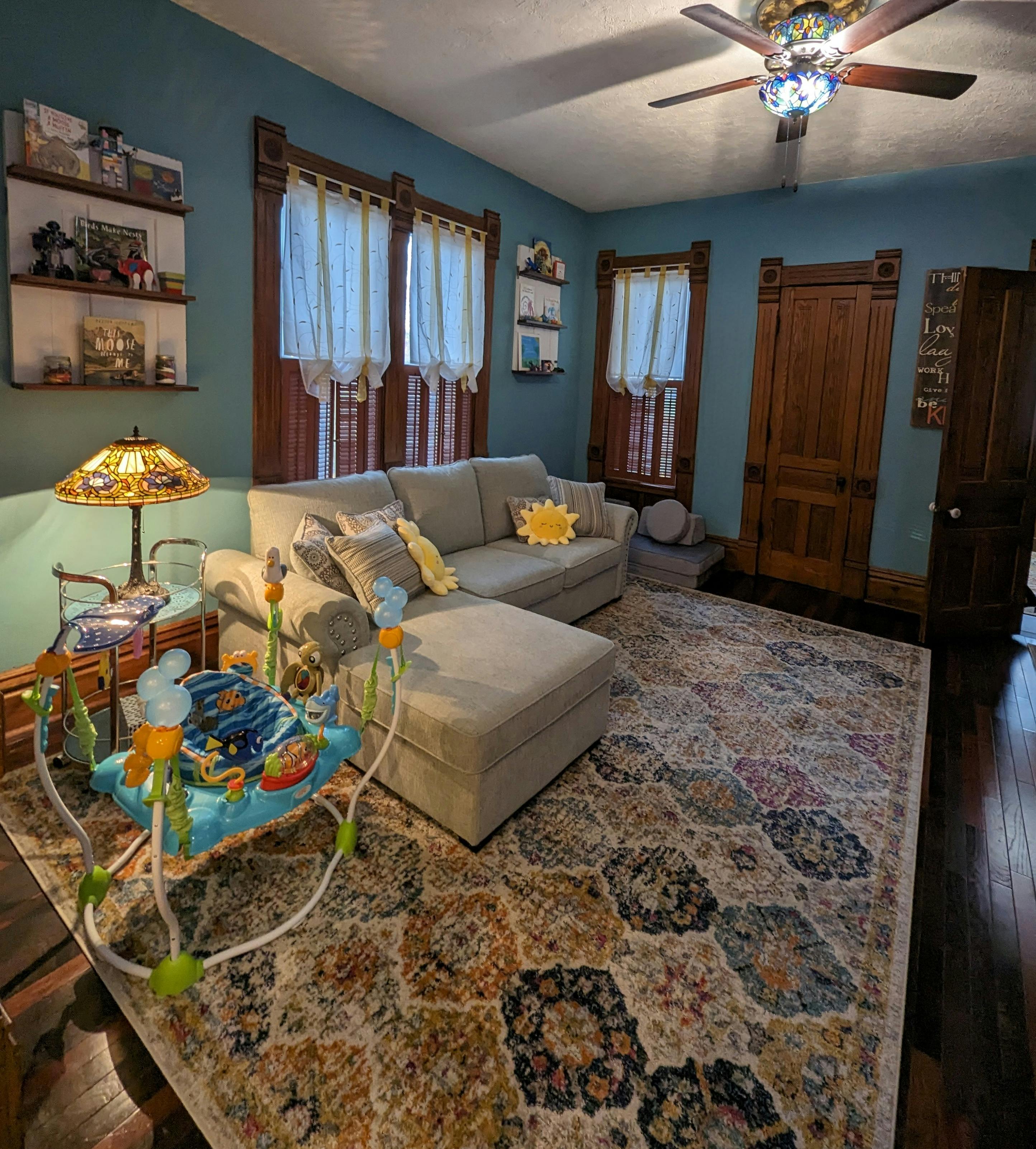 Living room with a sofa, ottoman, and baby bouncer on a patterned rug