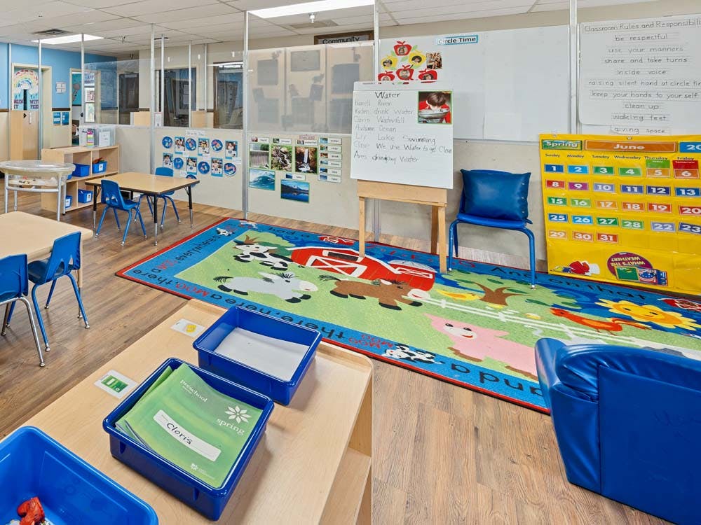 An empty early childhood education classroom with tables, chairs, and activity rugs