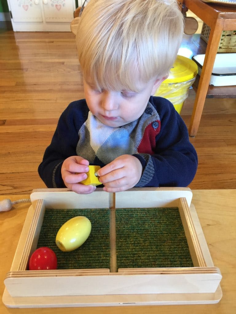 Child playing with a yellow block over a wooden tray with green felt