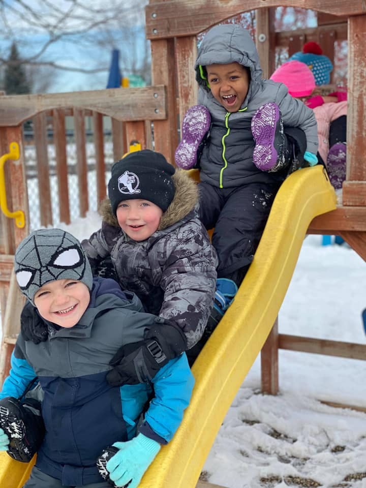 Three children on a playground slide in the snow