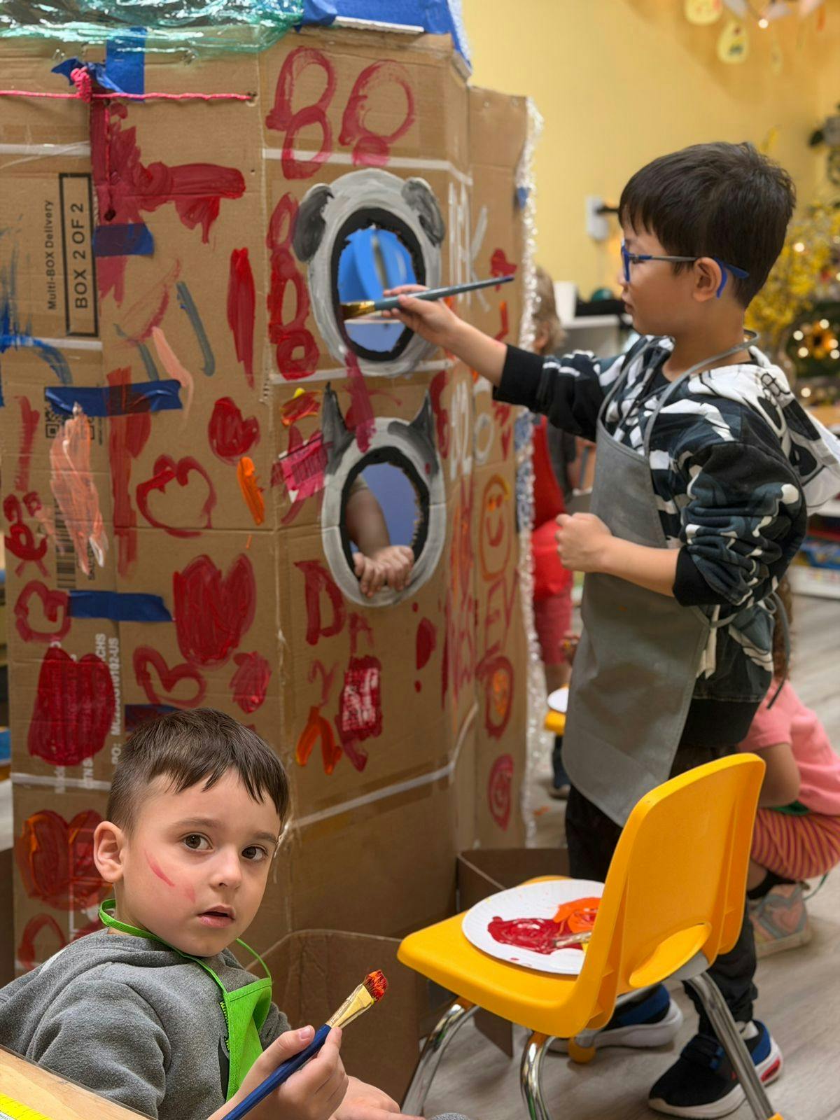 Children painting a cardboard structure in a classroom
