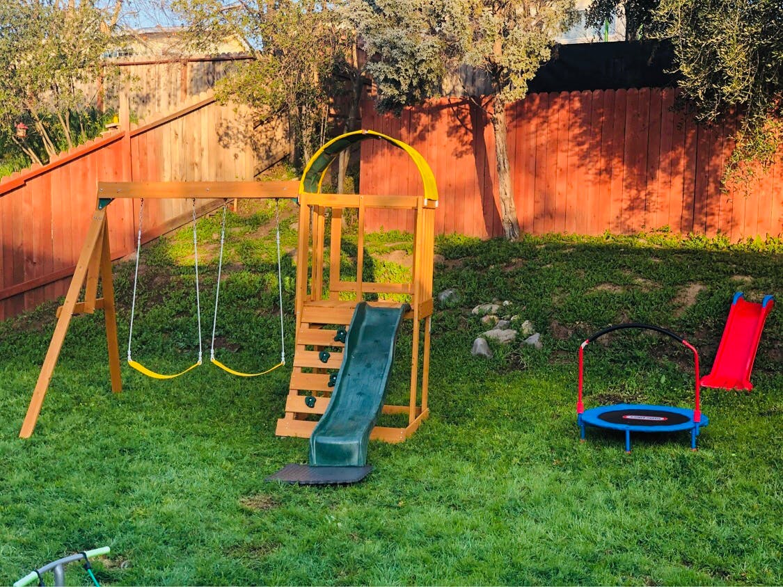 Wooden swing set with slide and two swings, small trampoline, and red slide