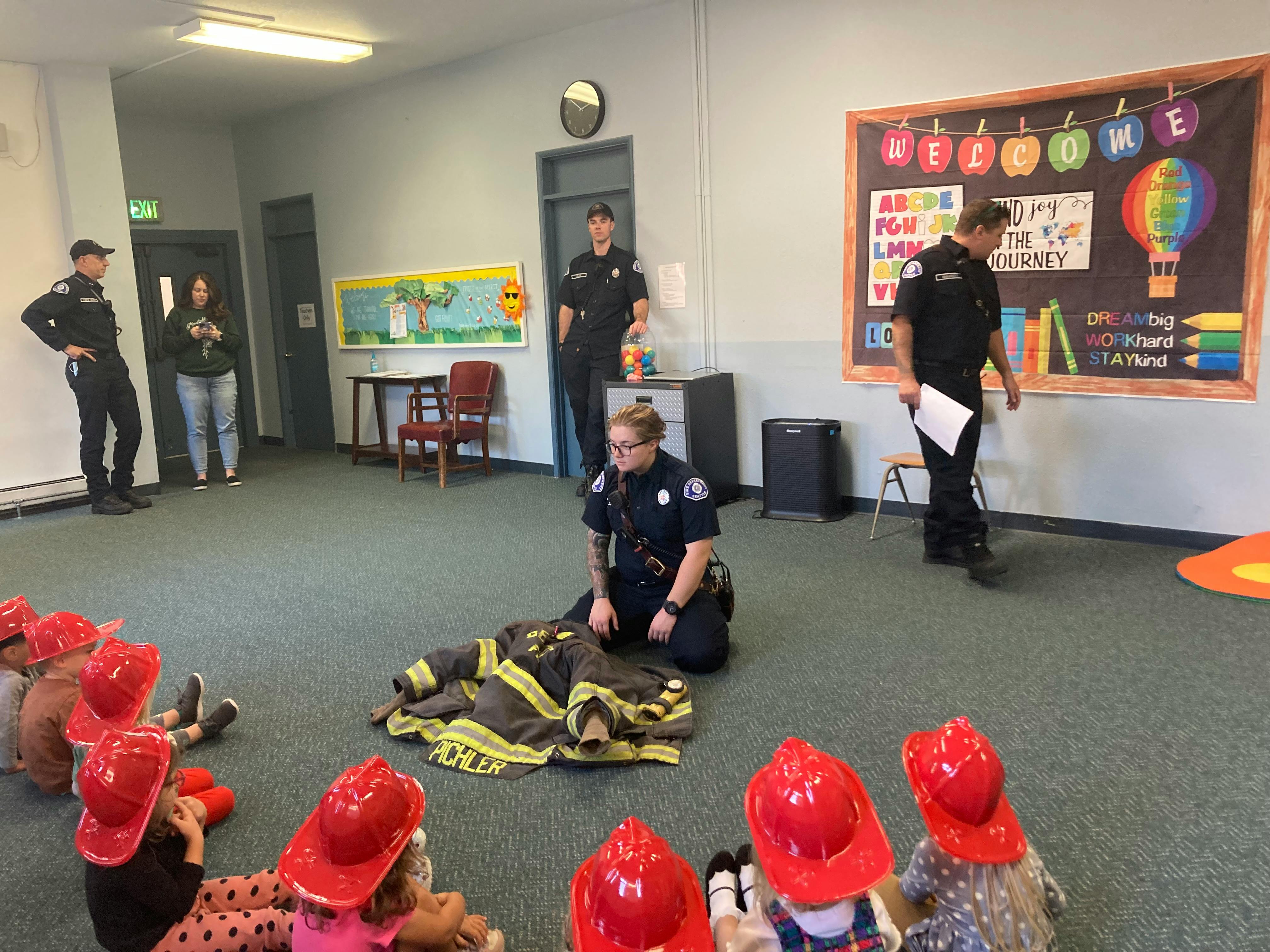 Person in uniform kneeling with firefighter gear in front of children