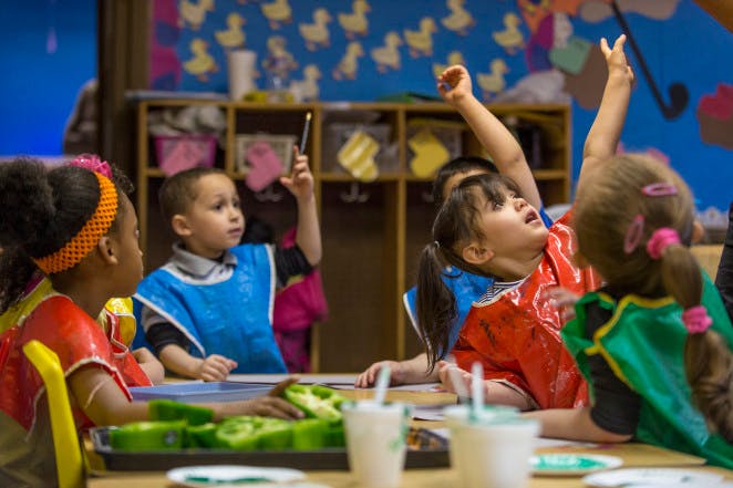 Children at a table, some raising their hands