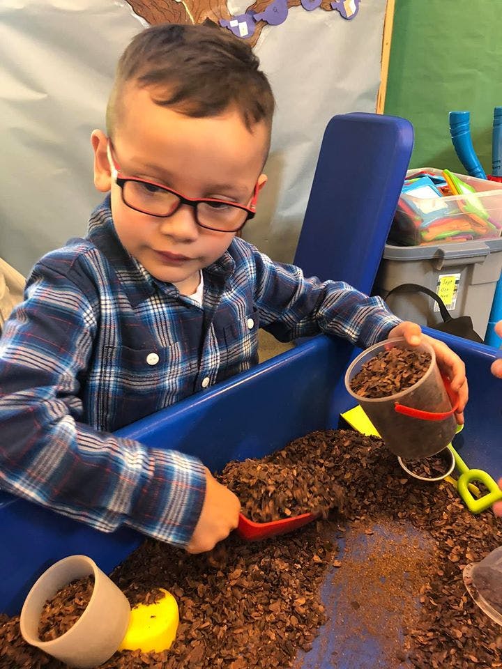 Child in glasses playing with wood chips and scoops