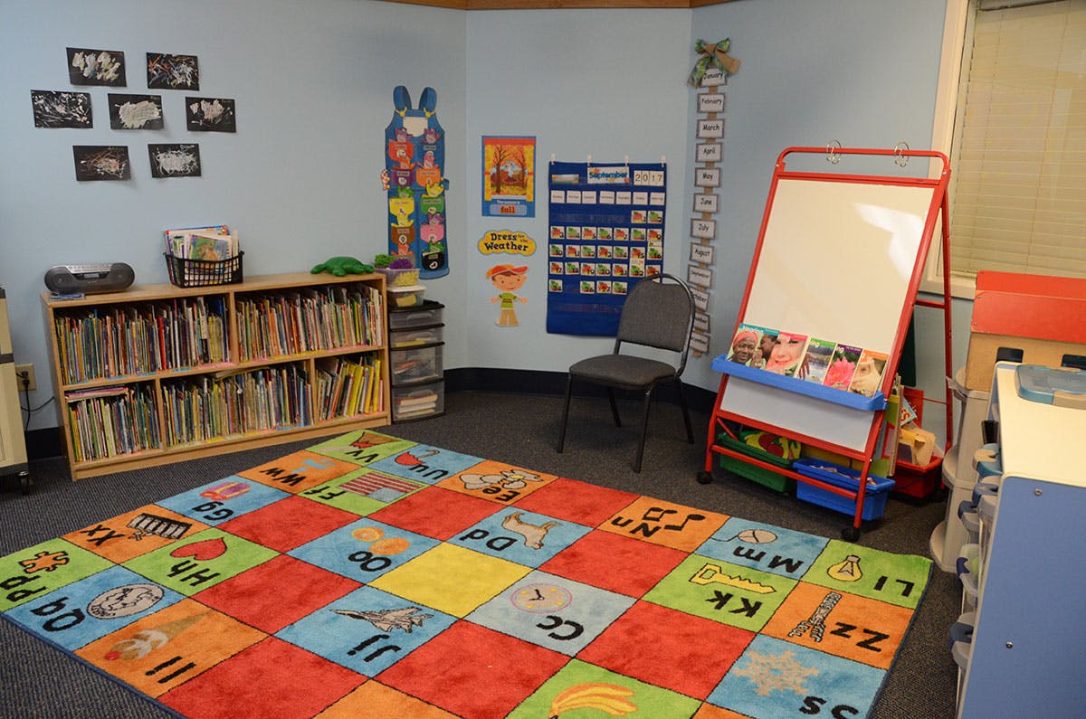 Colorful alphabet rug in a classroom with a bookshelf and whiteboard