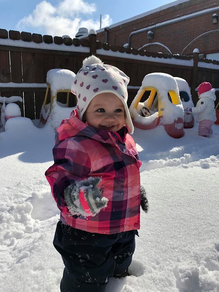 Child in a winter hat and plaid jacket standing in snow