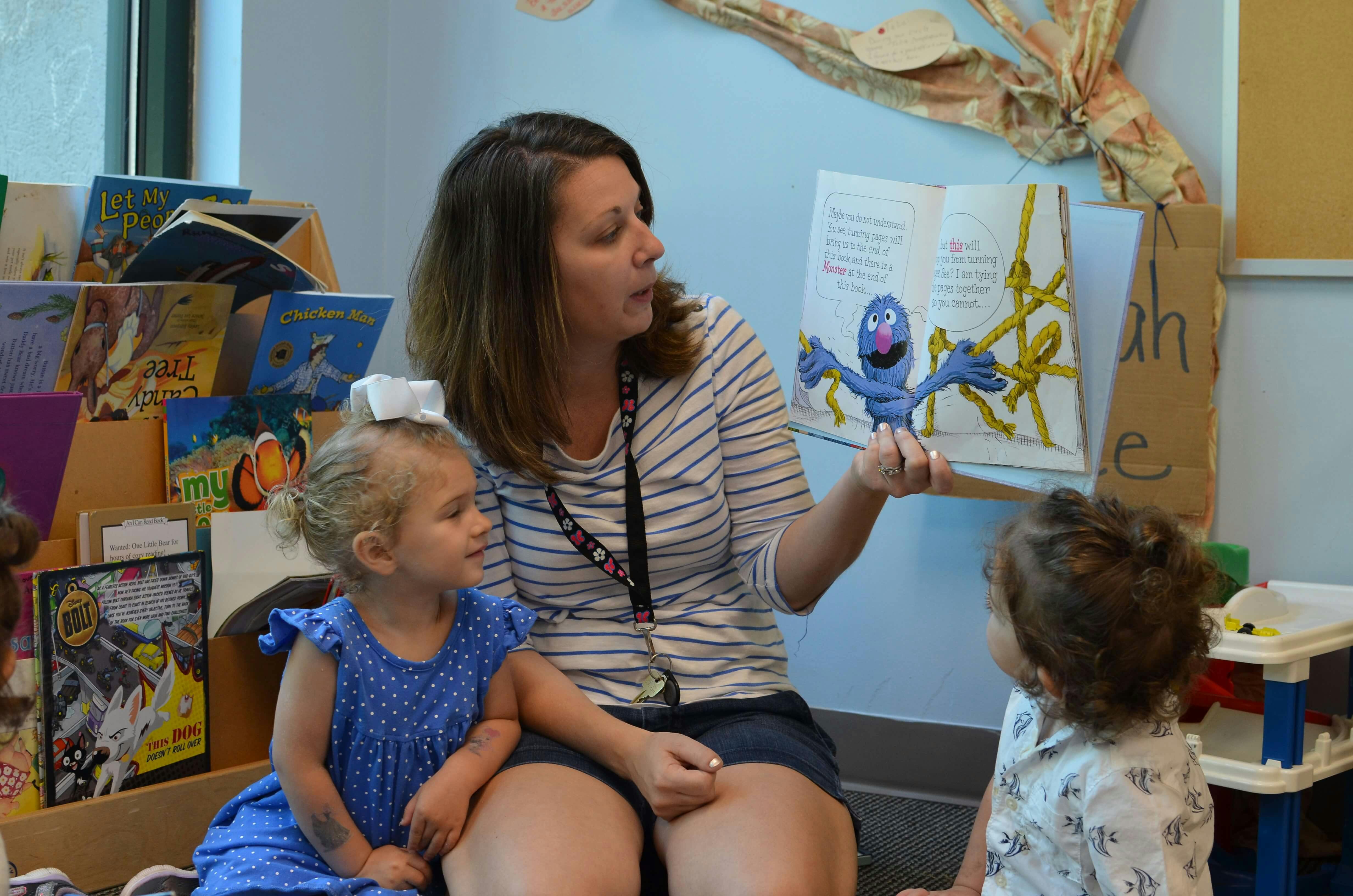 Person reading a book to two children, holding a puppet