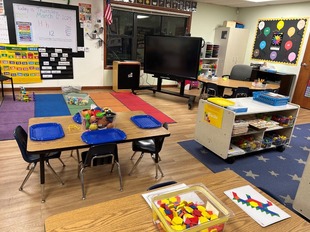 Classroom with small tables and chairs, whiteboards, and a screen