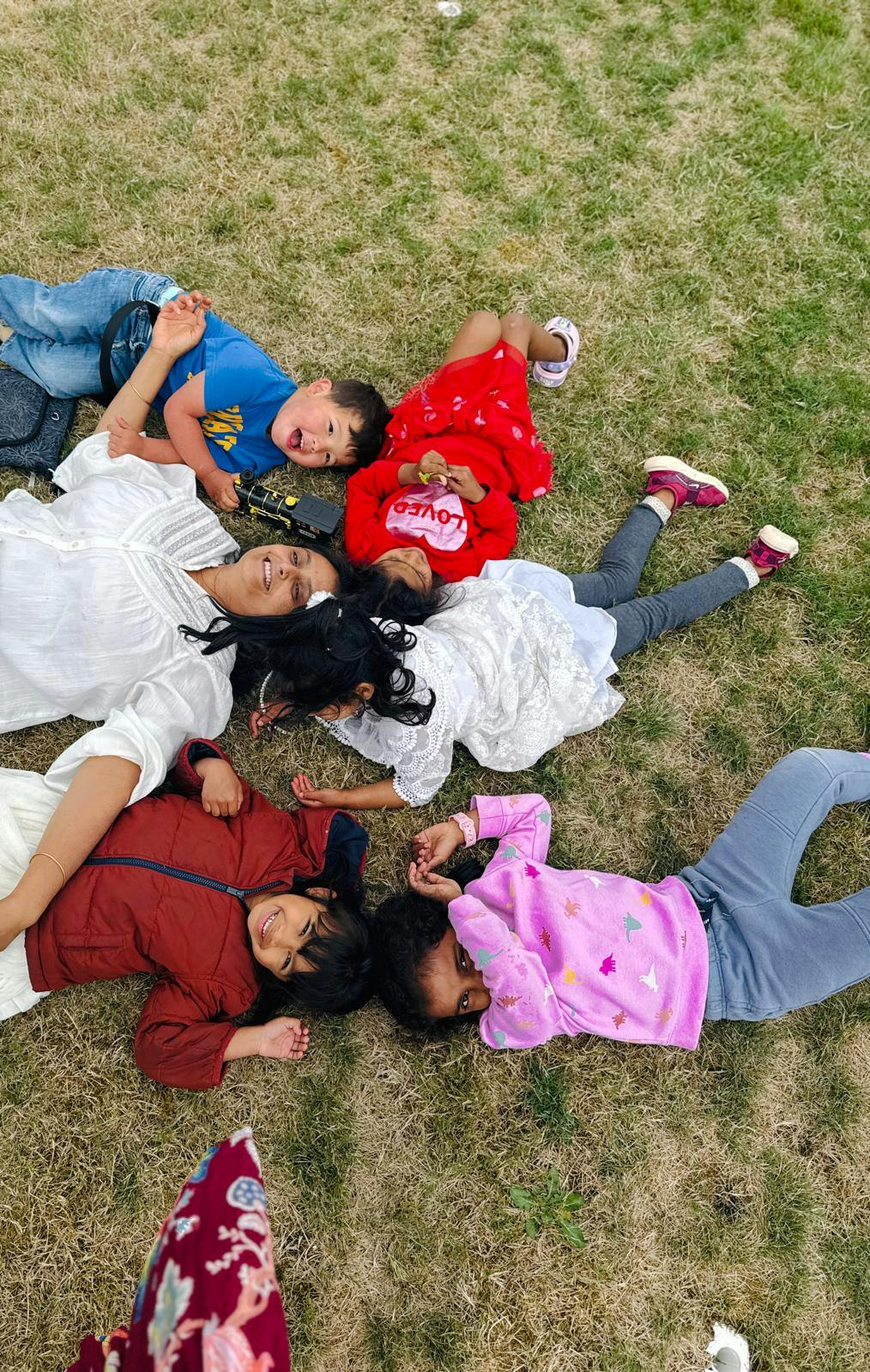 A person and four children lying in a circle on the grass