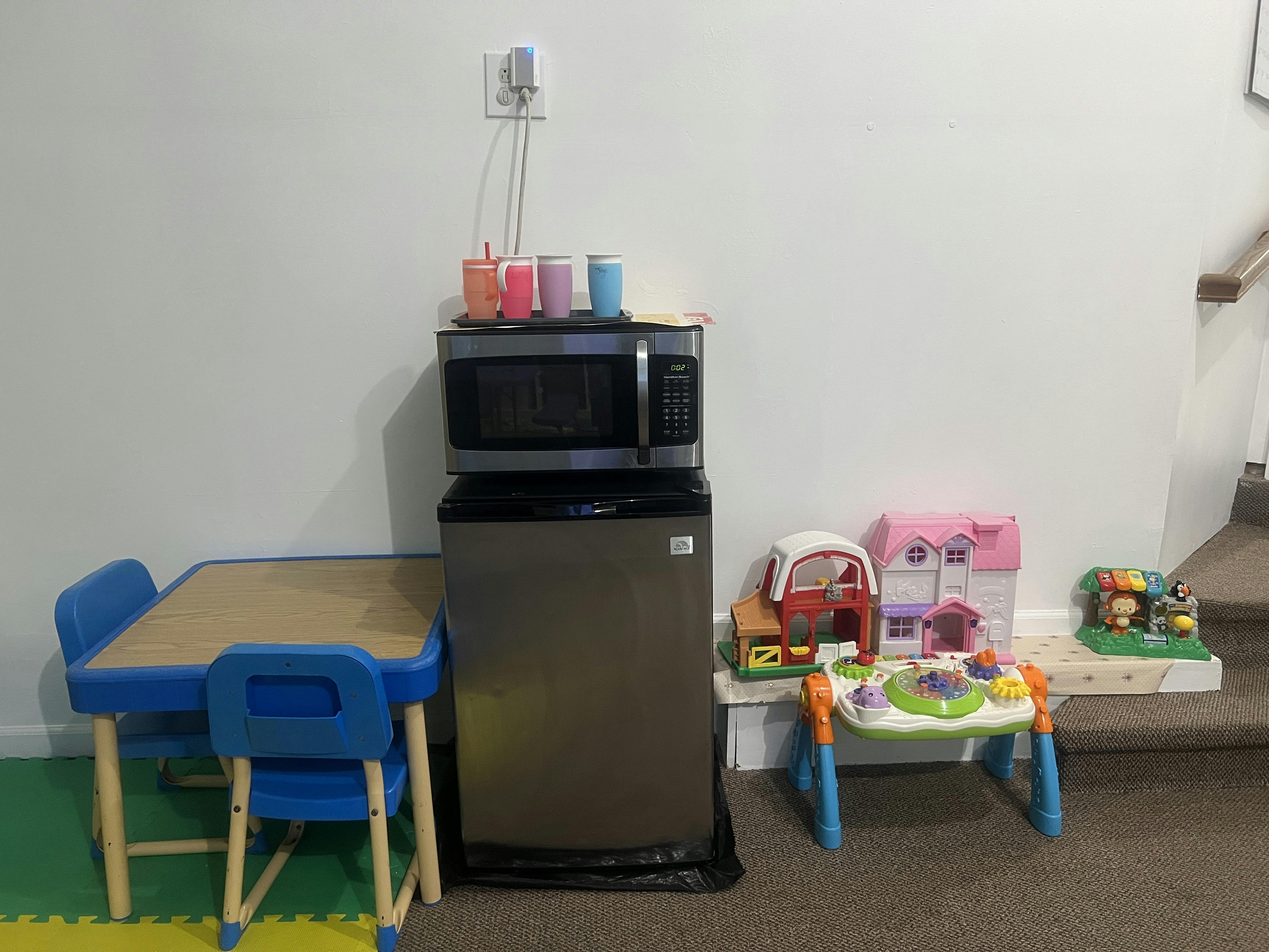 A children's table and chairs, microwave, mini-fridge, and toys on carpet