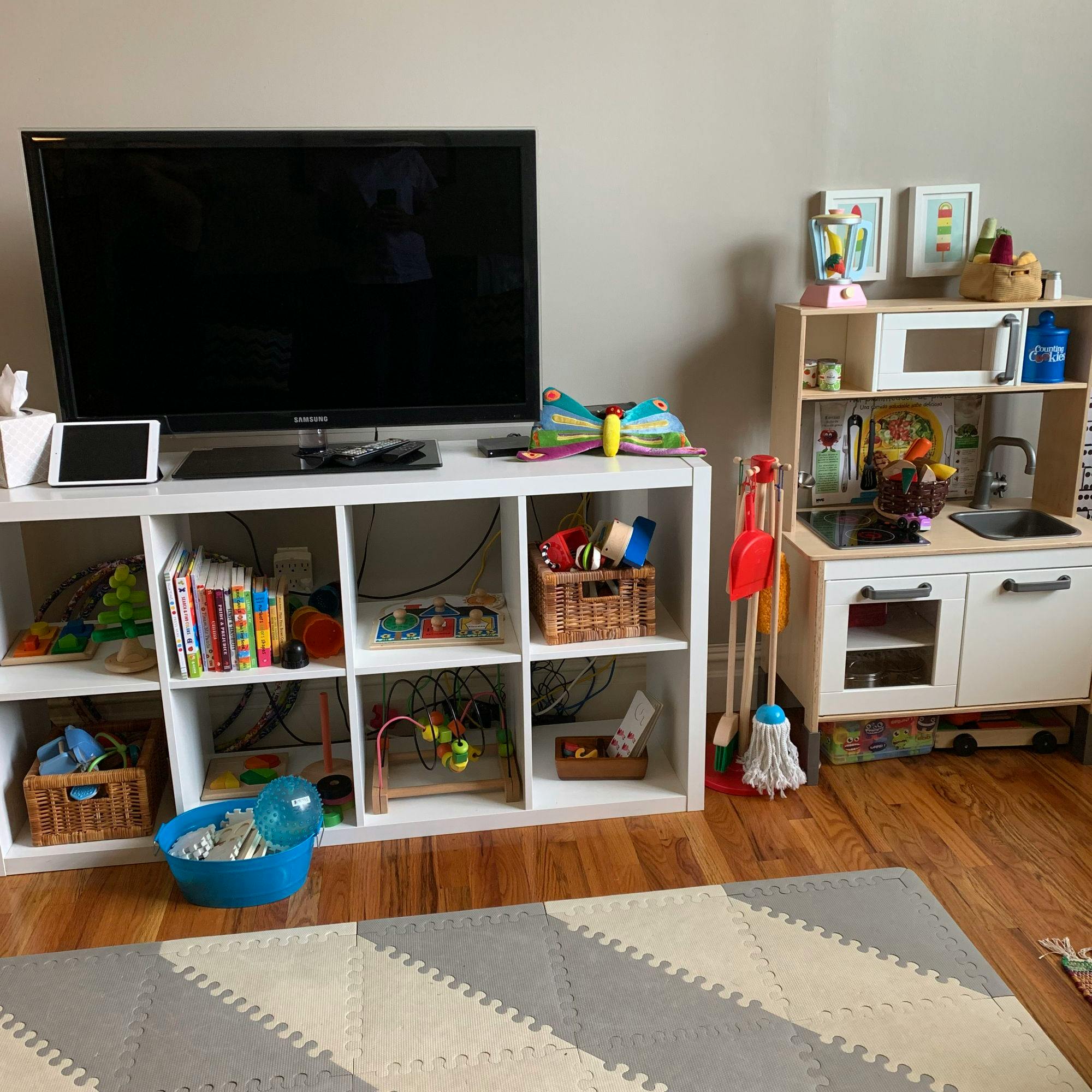 Living room with TV, storage unit with toys, and a child's play kitchen
