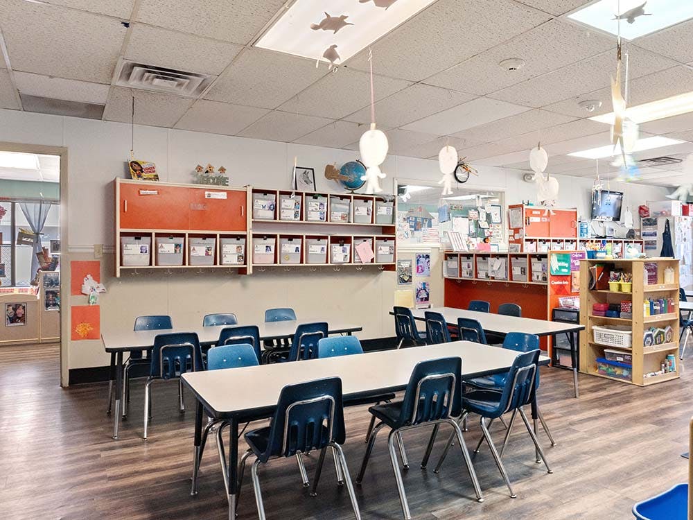 Classroom with tables and blue chairs, cubbies, and decorations