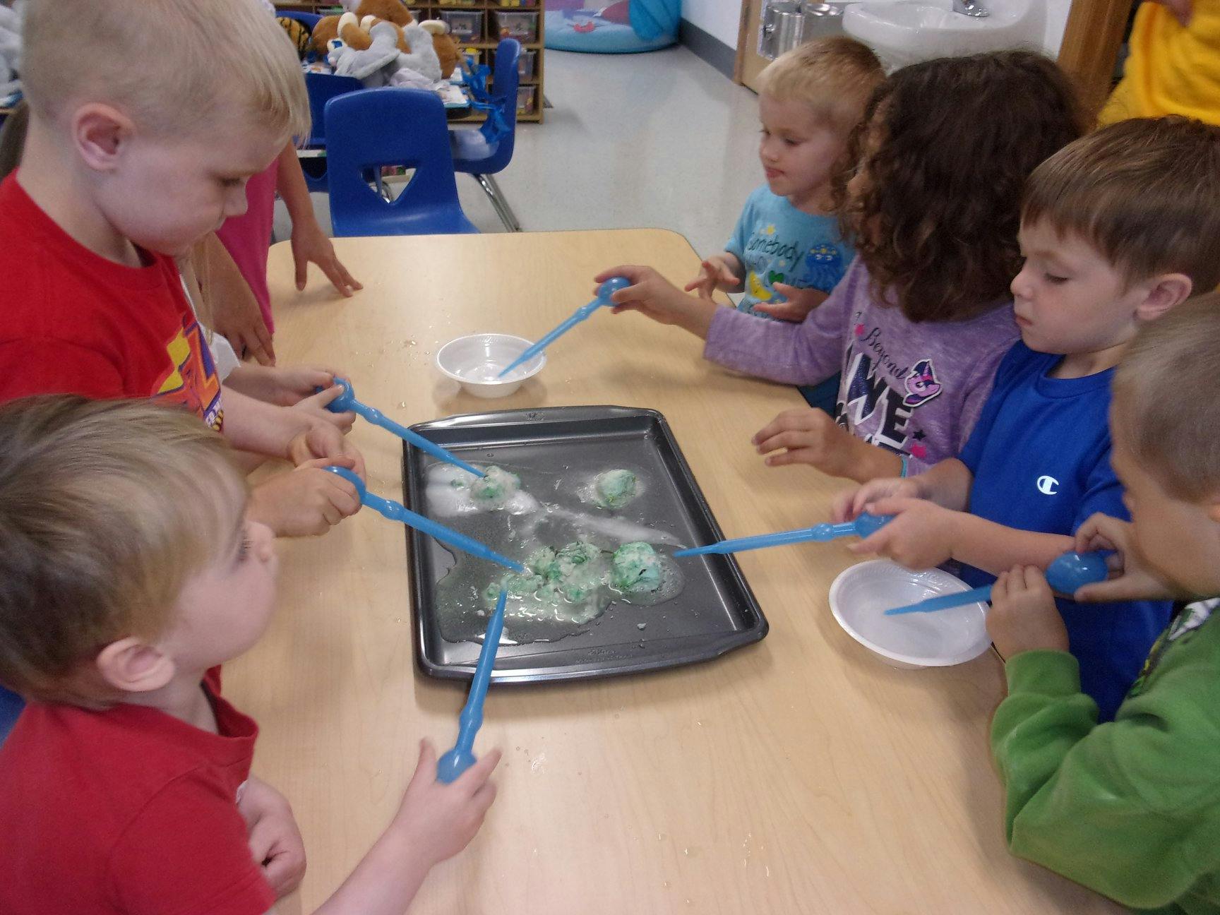 Children at a table playing with blue tools in a tray